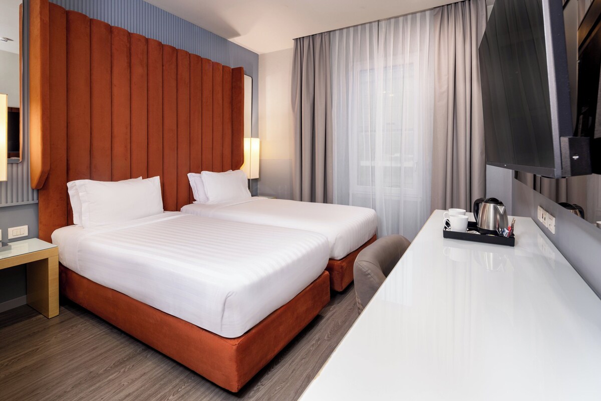 A hotel room with two beds, a desk, a TV, and a coffee tray.