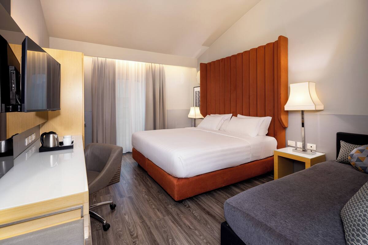 Quarto de hotel com cama, secretária com cafeteira, uma cadeira e televisão.