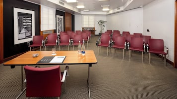 A conference room with a long table, red chairs, a projector screen, and a plant.