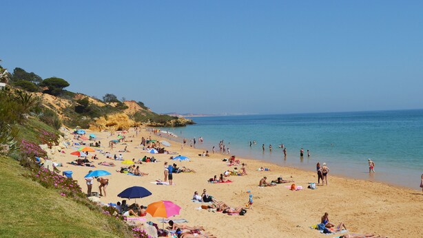 A beach with people sunbathing and swimming, and umbrellas providing shade. - Urban Hotel Santa Eulália (Albufeira)