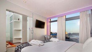 A hotel room with a bed, a TV mounted on the wall, a chair, and a large window with curtains. - Urban Hotel Santa Eulália (Albufeira)