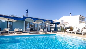 A swimming pool with lounge chairs and umbrellas, a clear blue sky, and a building with a white facade and blue accents. - Urban Hotel Santa Eulália (Albufeira)