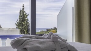 A neatly folded white towel on a bed with a view of the sea and a tree through a window. - Urban Hotel Santa Eulália (Albufeira)