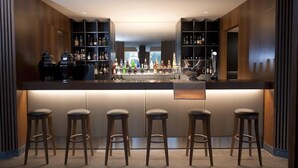 Un espace bar moderne doté d’un comptoir central, de tabourets et d’étagères remplies de bouteilles.