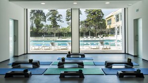 Une salle de remise en forme équipée de matériel d’exercice et de tapis, avec de grandes fenêtres donnant sur un espace piscine.