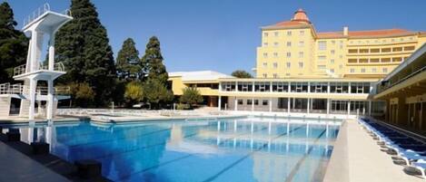 A swimming pool with diving platforms and a large building in the background.
