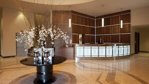 Un hall d’hôtel moderne avec un comptoir d’accueil, un grand vase rempli de fleurs blanches et un sol en marbre.