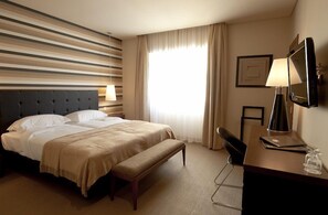 Una habitación de hotel con una cama grande, un escritorio con lámpara, televisión y ventana con cortinas.