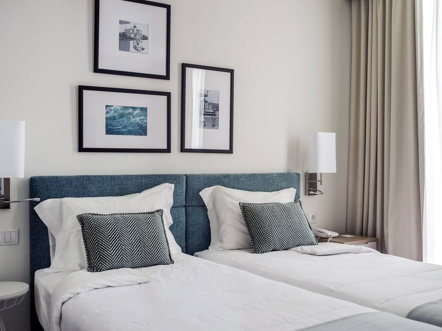 Une chambre d’hôtel avec deux lits, une tête de lit bleue, du linge de lit blanc et trois tableaux encadrés accrochés au mur.
