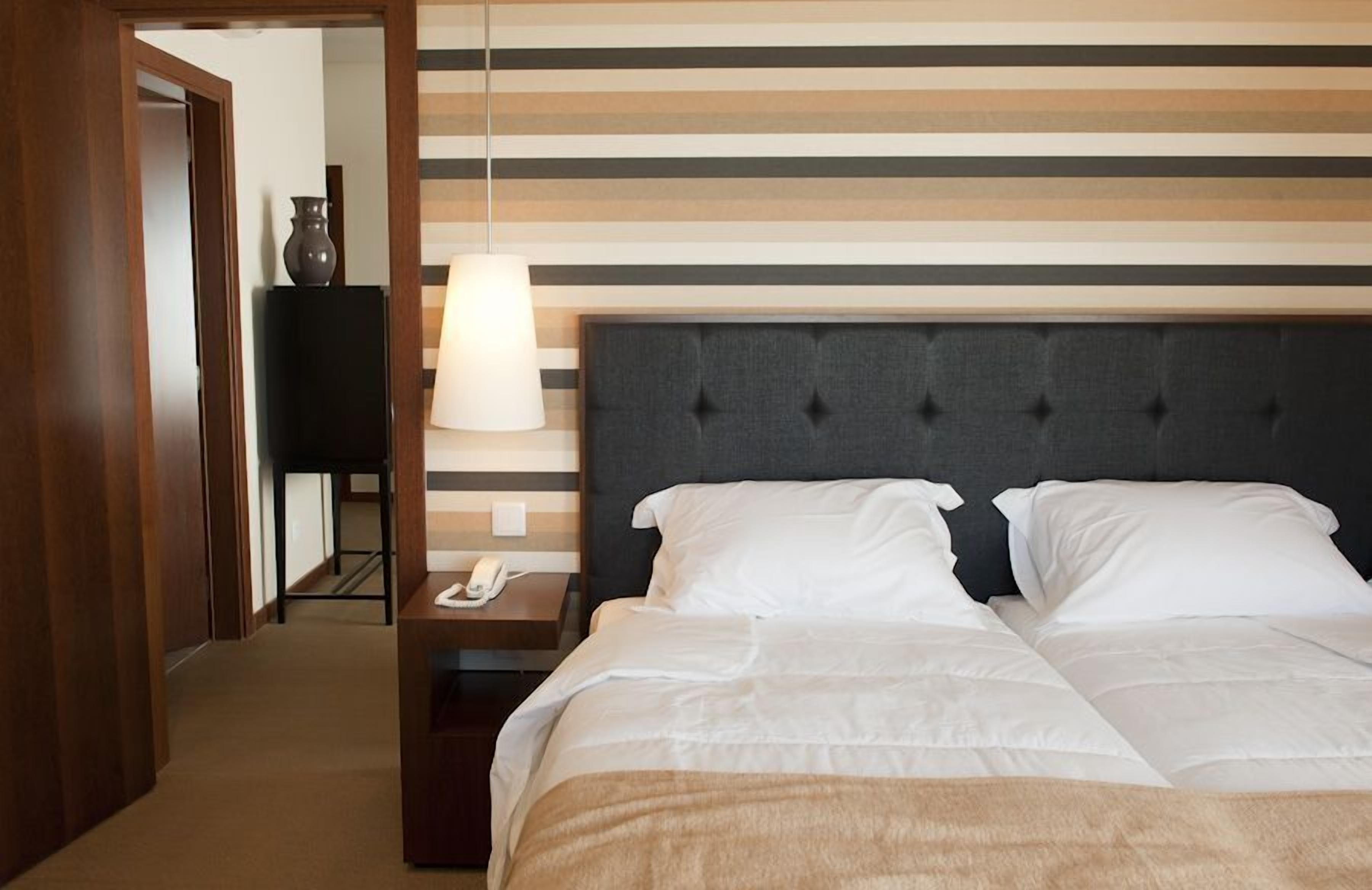 A hotel room with a bed, a bedside table with a lamp, and a telephone.