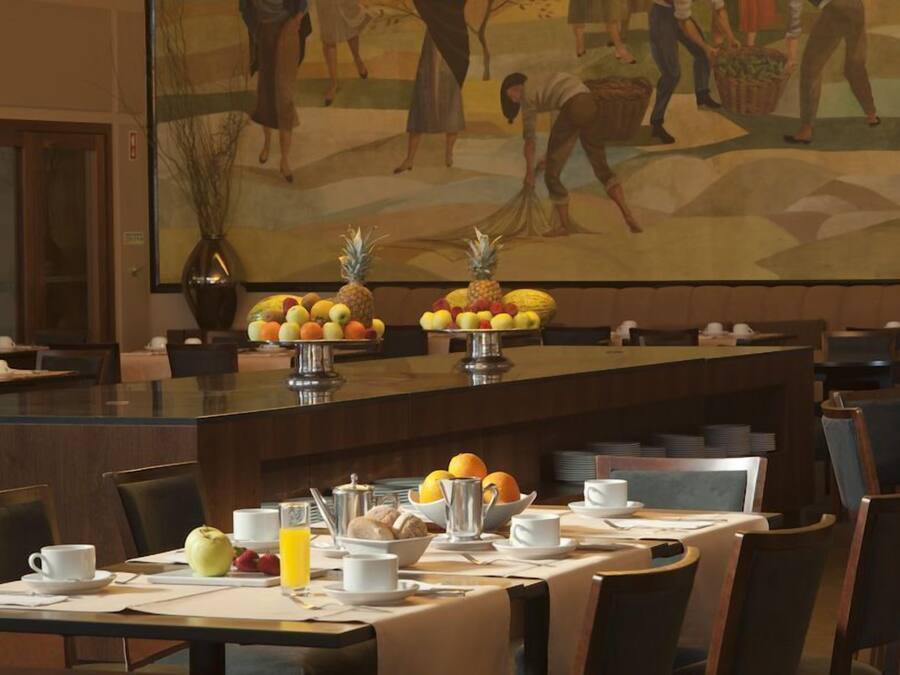 Een restaurantgedeelte van een hotel, met gedekte tafels voor het ontbijt, met fruit, gebak en koffie.