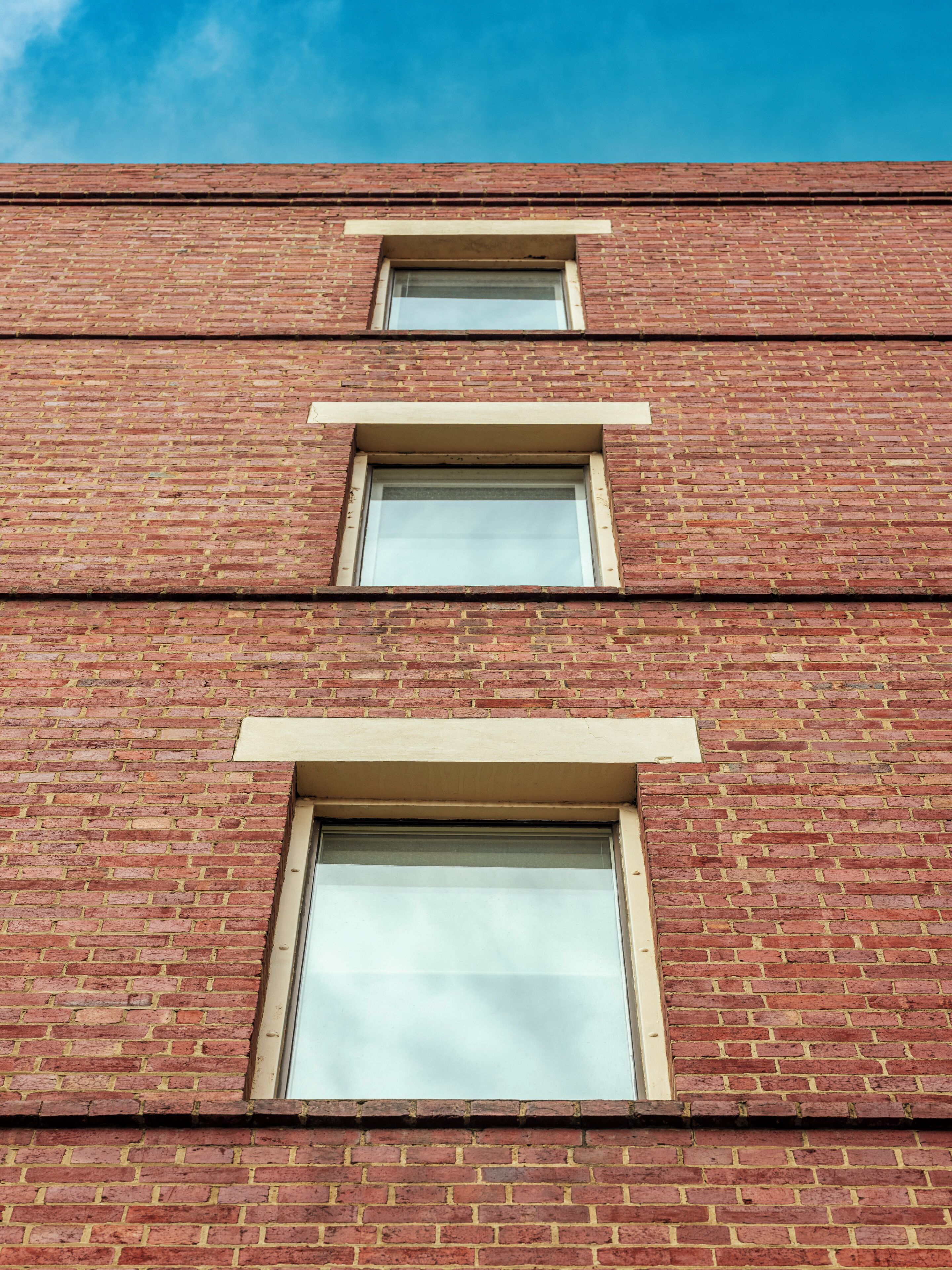 Un immeuble en briques à plusieurs étages, avec trois fenêtres alignées verticalement.