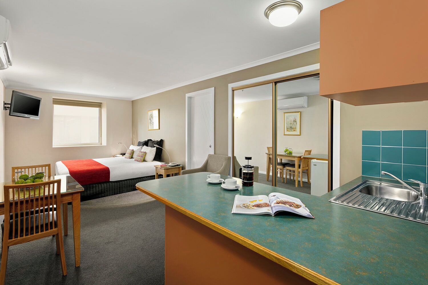 Habitación de hotel con cama, escritorio, silla, mesa de comedor, cafetera y lavabo.
