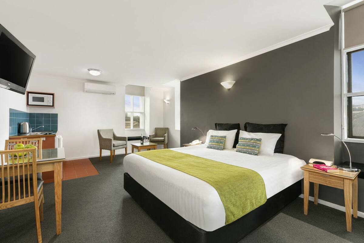 A hotel room with a bed, a desk, a chair, a TV, a microwave, and a window.