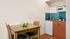 A compact kitchen with a microwave, coffee maker, and a small sink. There is a dining table with chairs and a fruit basket. - Hobart Waterfront Apartments (Hobart)