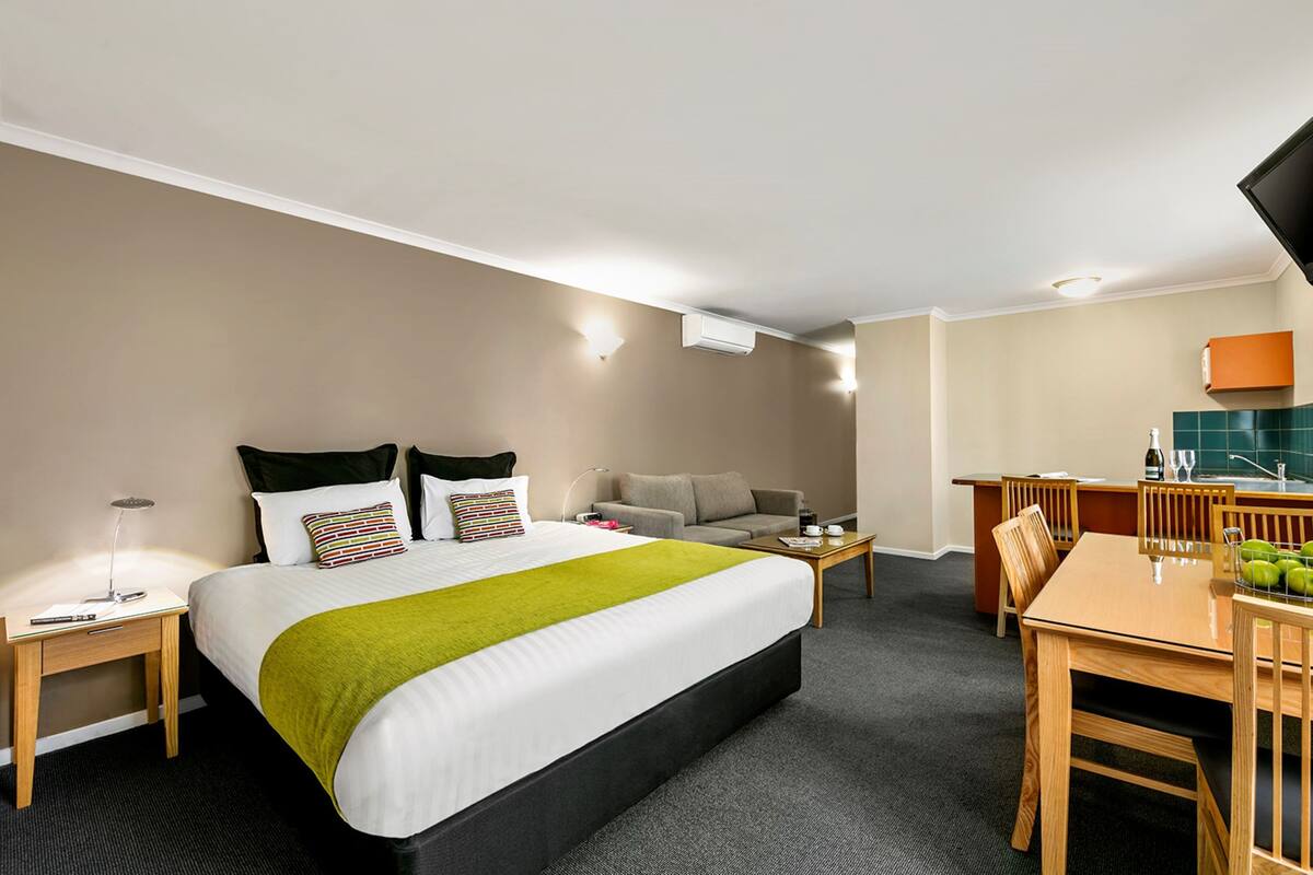 A hotel room with a bed, a desk, a chair, a sofa, a dining table, and a TV.