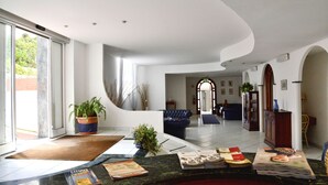 Eine geräumige Lobby mit gewölbter Decke, einem Empfangstresen mit Zeitschriften, einem blauen Sofa und einem Blumentopf.