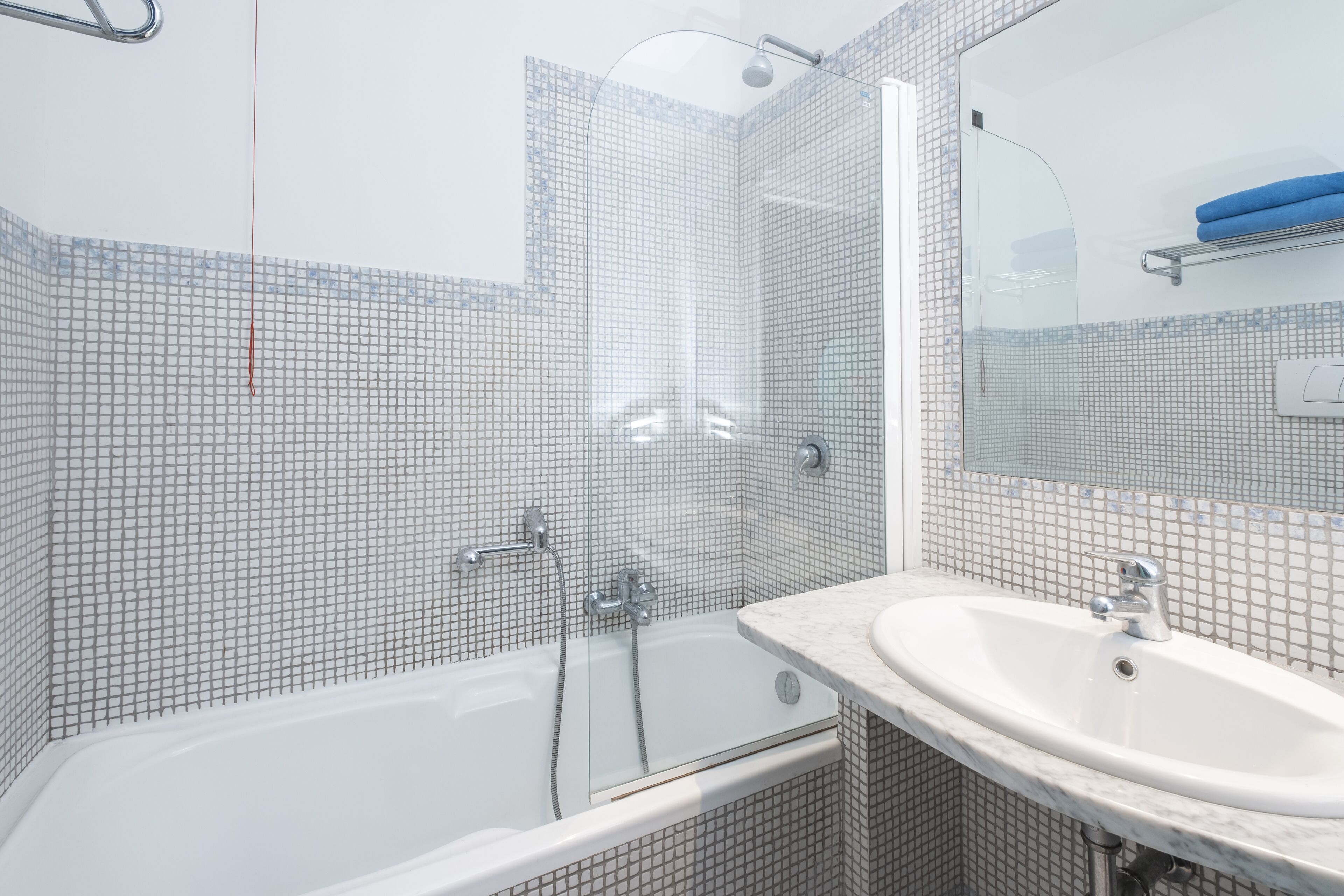Un baño con ducha de vidrio, un lavamanos blanco y pared de azulejos.