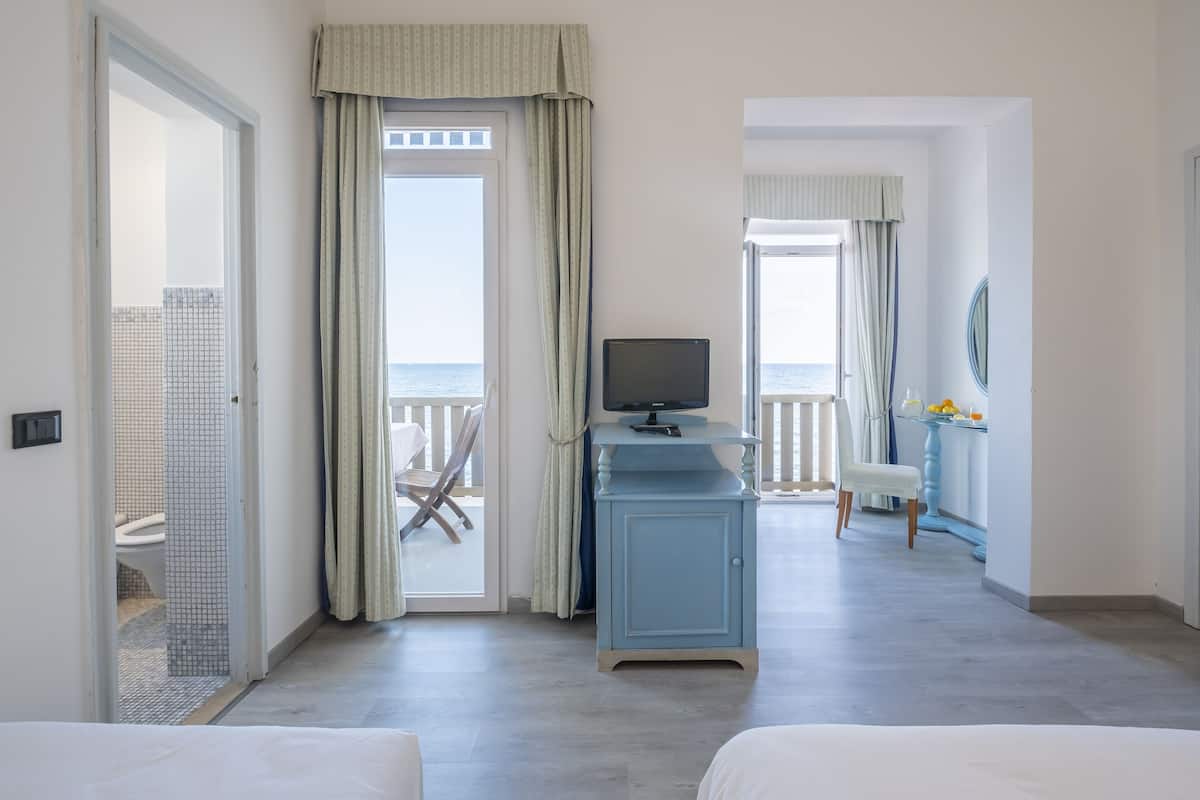 A hotel room with a balcony, a television on a cabinet, and a view of the sea.