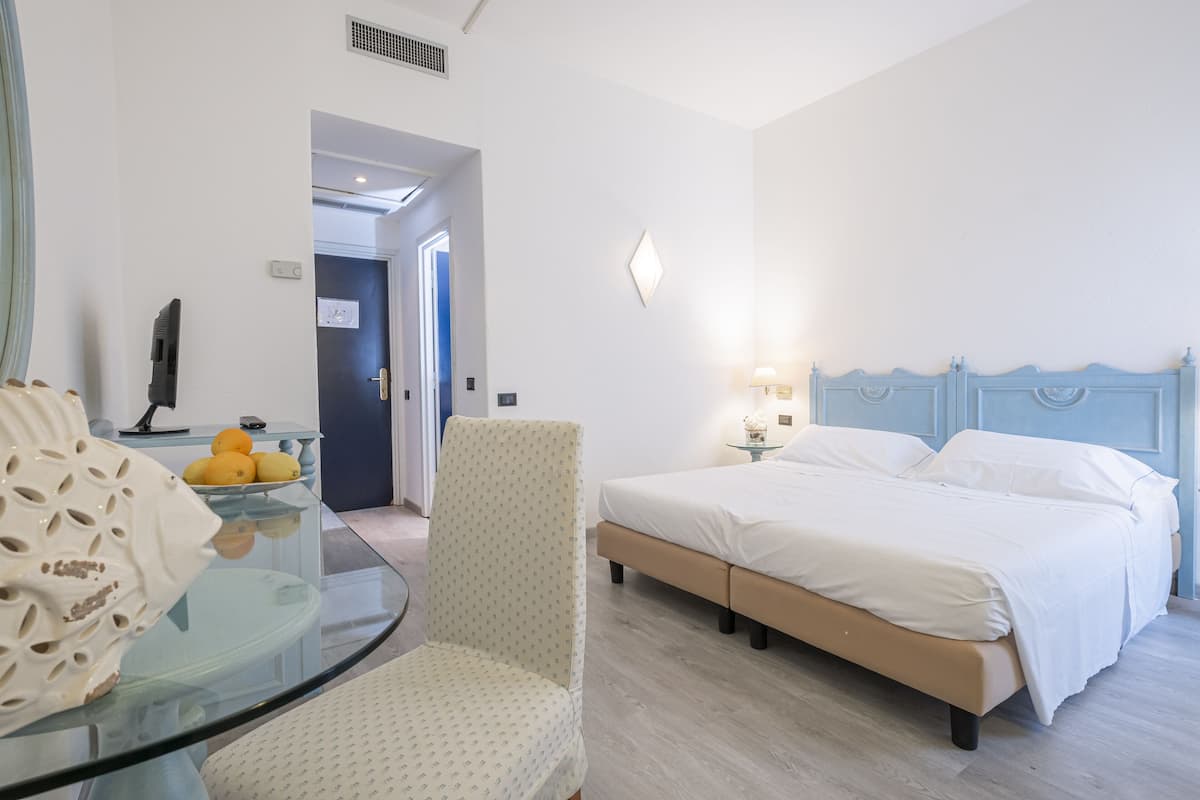 A hotel room with a bed, a chair, a glass table with fruits, and a lamp.