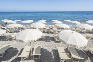 A beach with numerous white umbrellas and sun loungers arranged on a pebbled surface. - Hotel del Sole (Santa Marinella)