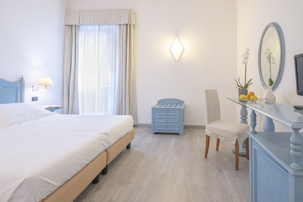 A hotel room with a bed, a desk with a mirror, a chair, and a small table with flowers and fruit. - Hotel del Sole (Santa Marinella)