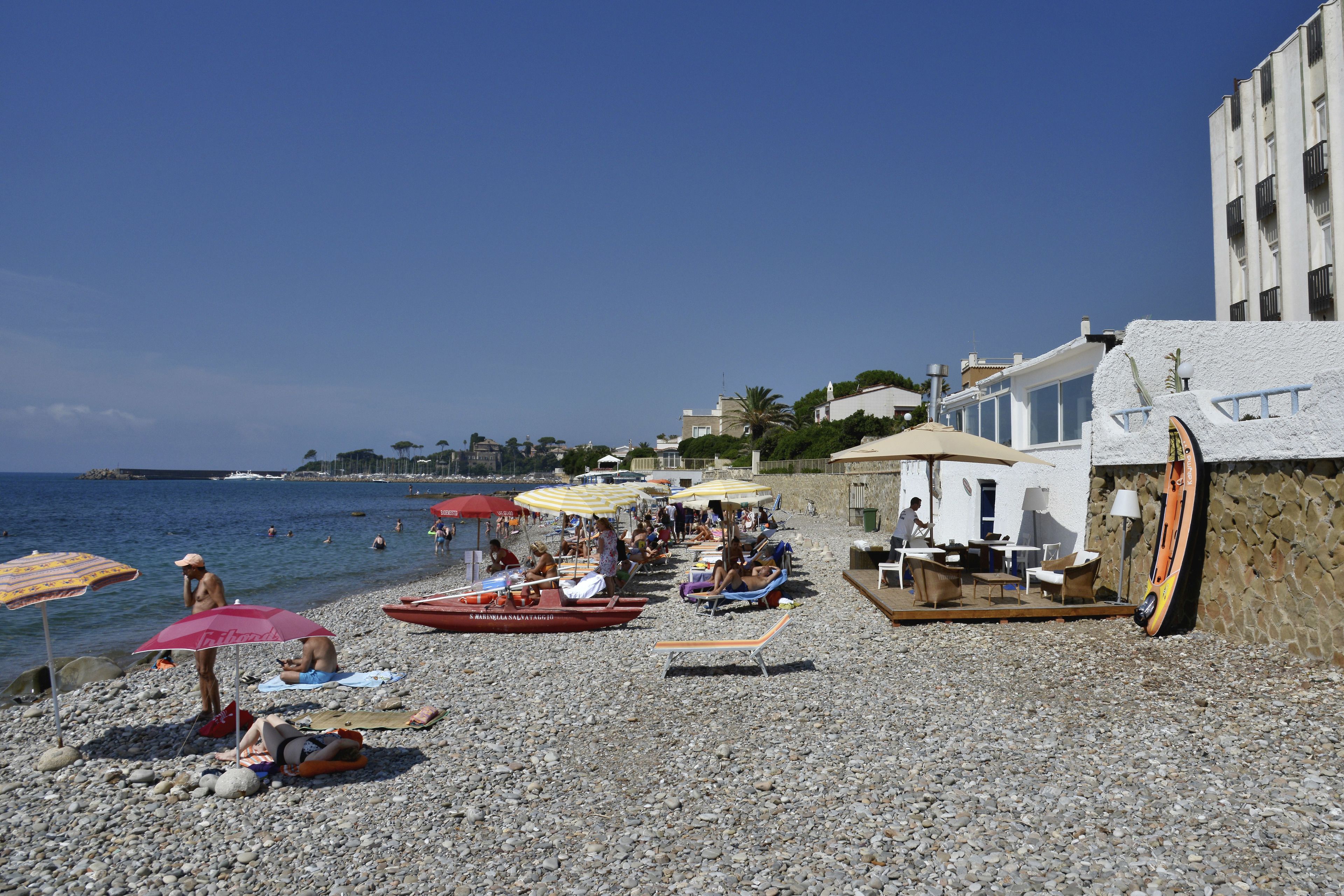 A pebbled beach with umbrellas, lounge chairs, and a building with a white facade.