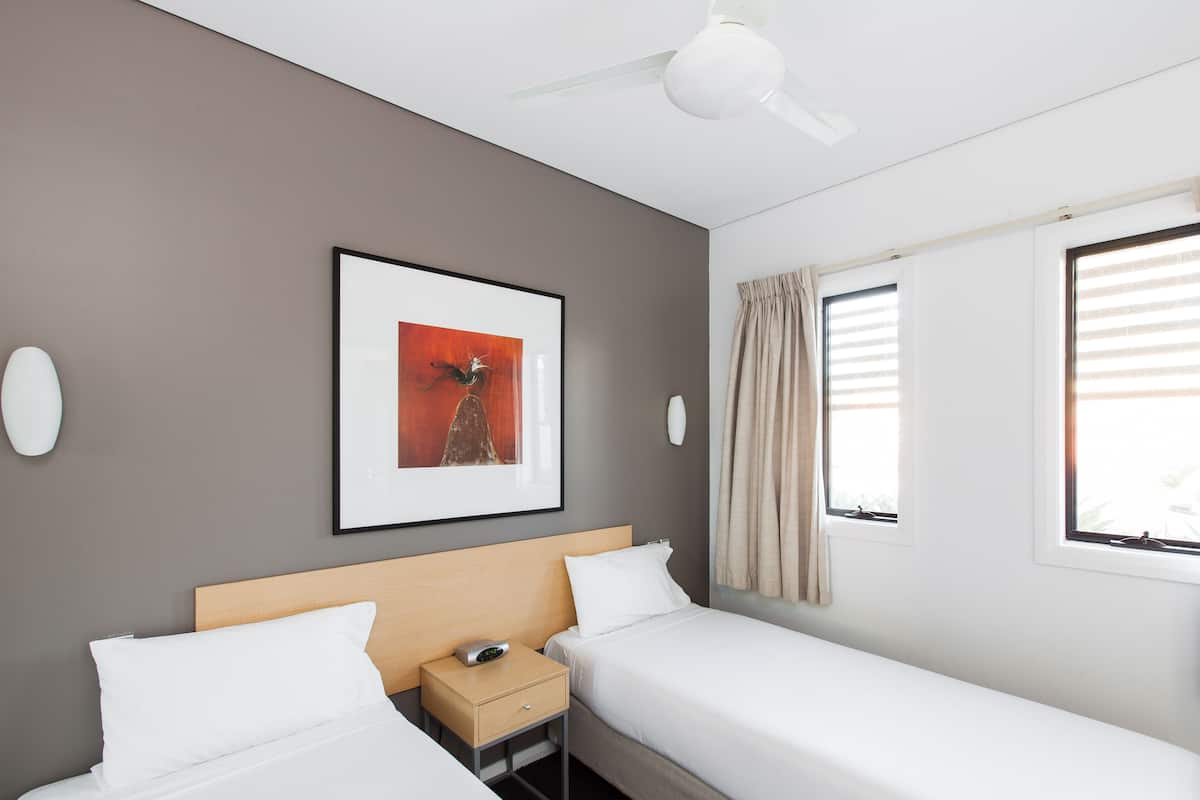 Ein Hotelzimmer mit zwei Einzelbetten, einem Nachttisch mit Lampe, einem Deckenventilator und einem gerahmten Bild an der Wand.