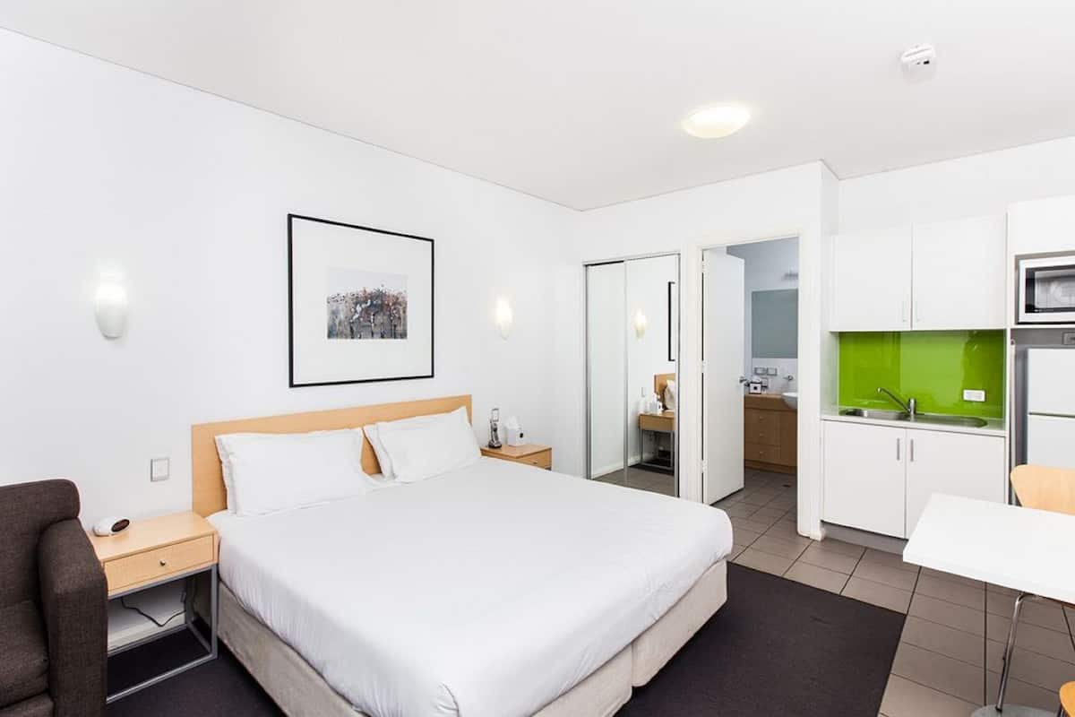 Ein Hotelzimmer mit einem großen Bett, einem Schreibtisch, einem Stuhl, einer Küchenzeile und einem durch eine geöffnete Tür einsehbaren Badezimmer.
