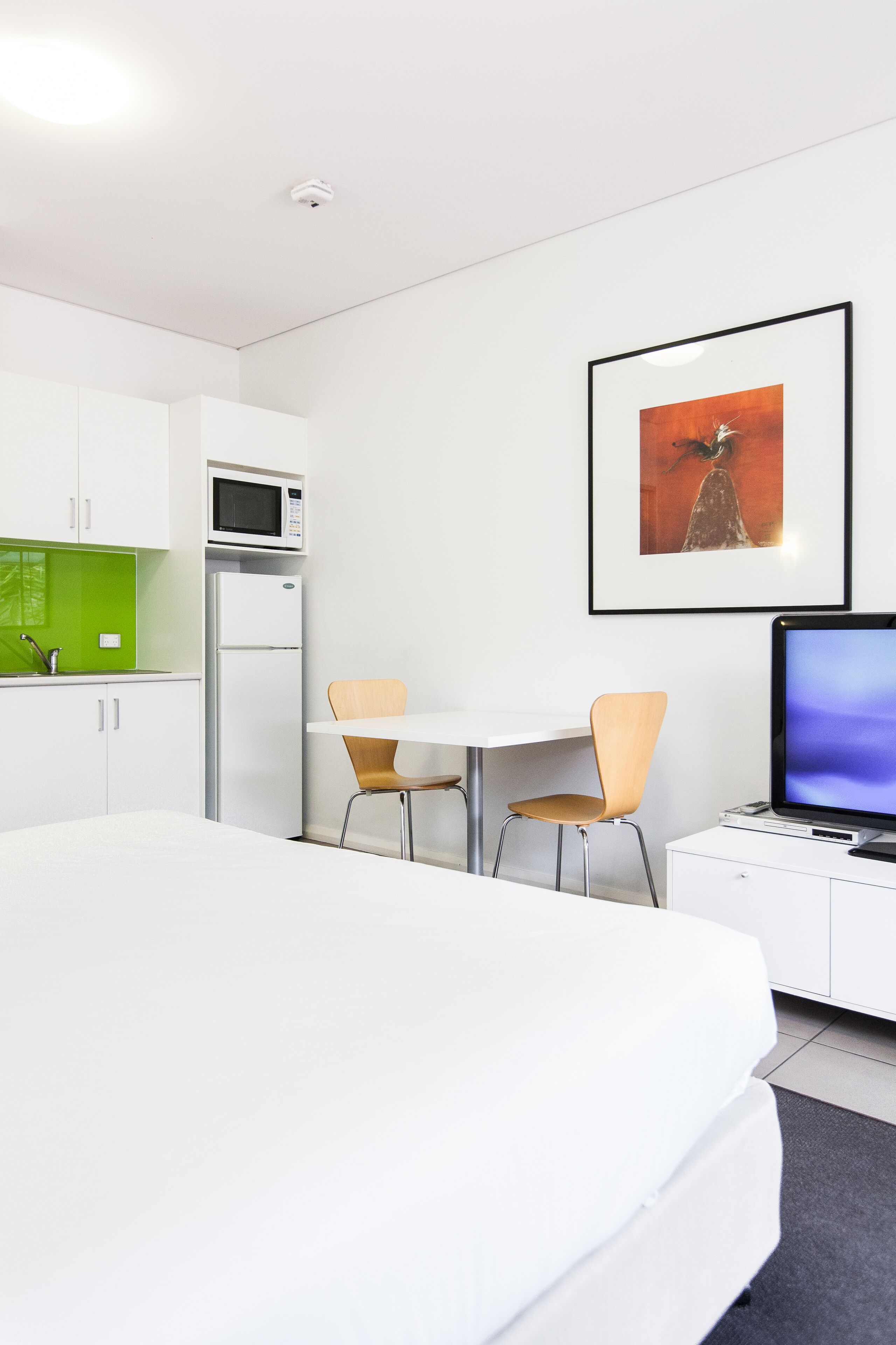 Moderni hotellihuone, jossa on sänky, työpöytä tietokoneella, mikroaaltouuni ja jääkaappi.