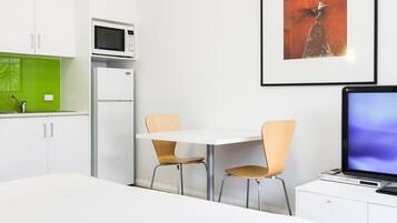 Moderni hotellihuone, jossa on sänky, työpöytä tietokoneella, mikroaaltouuni ja jääkaappi.