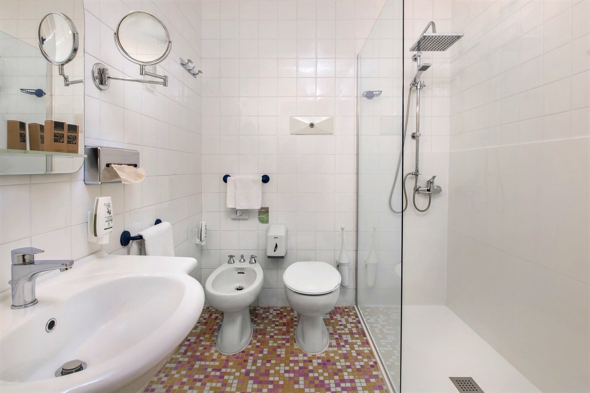 A modern bathroom with a white sink, two toilets, a bidet, and a shower.