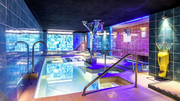 A modern indoor pool area with clear water, metal railings, and a tiled wall with a poster. - Hotel Santoli (Alto Reno Terme)