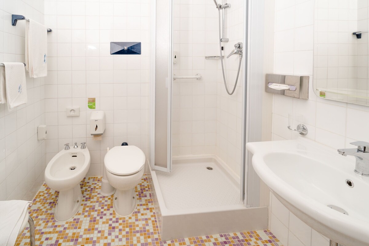 A bathroom with two toilets, a bidet, a shower, and a sink.