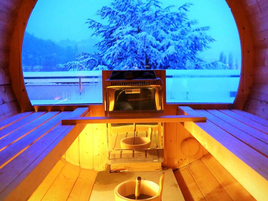 Un sauna avec un banc en bois et une vue sur un paysage enneigé, visible à travers une grande fenêtre en arc de cercle.