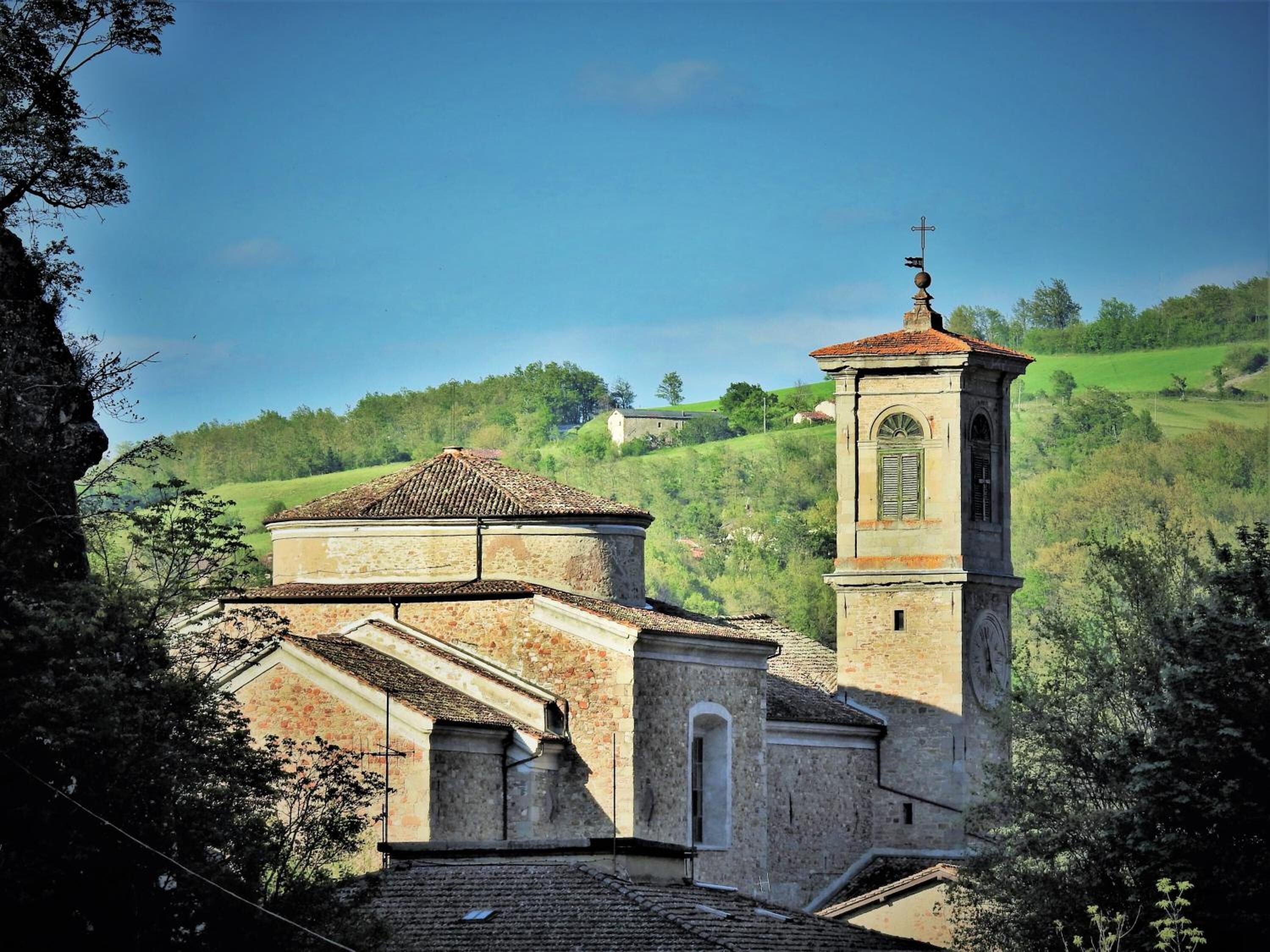 Uma igreja com uma torre de sino e telhado de azulejos, rodeada por vegetação e colinas.