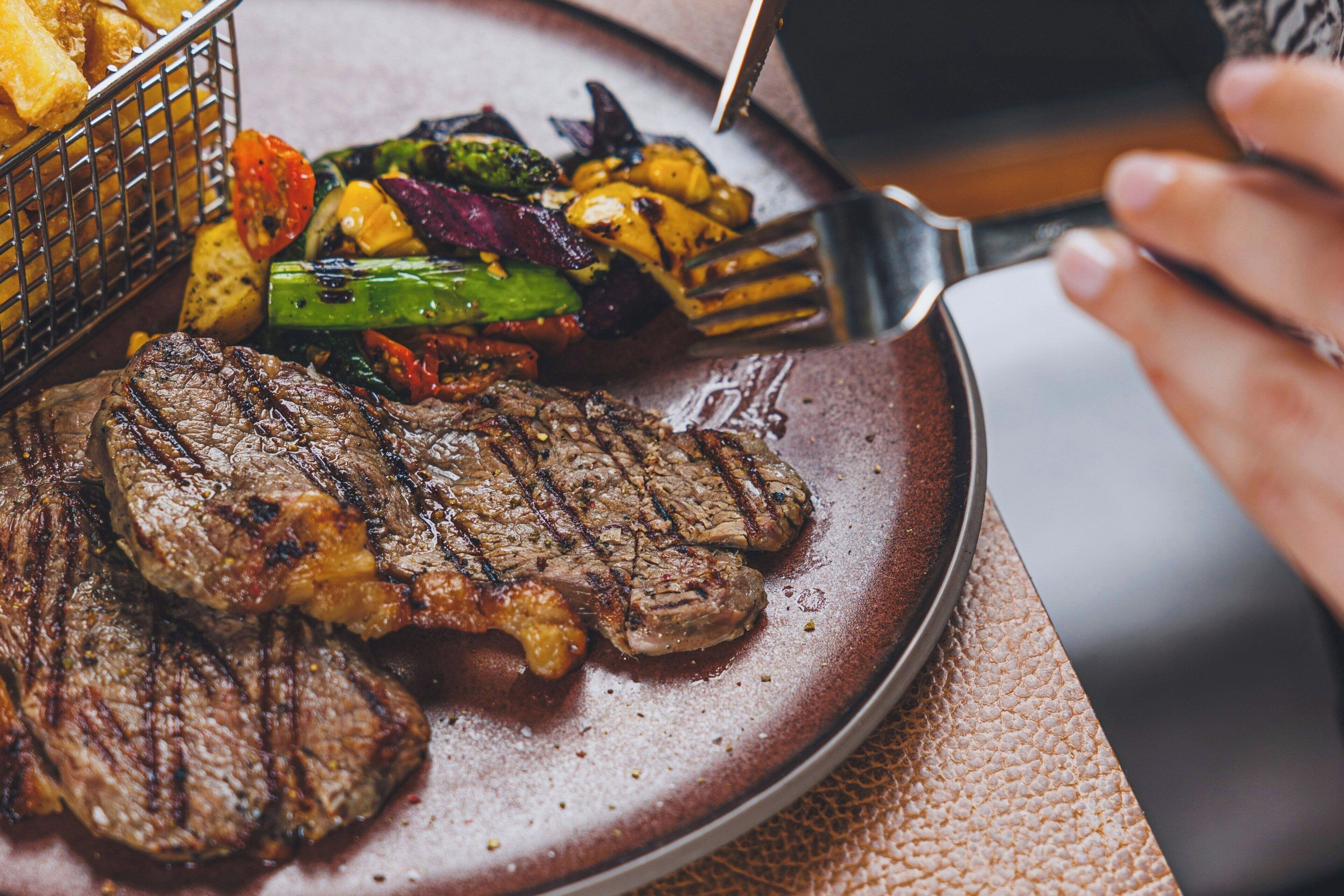 A plate of grilled steak with vegetables and a basket of fries.