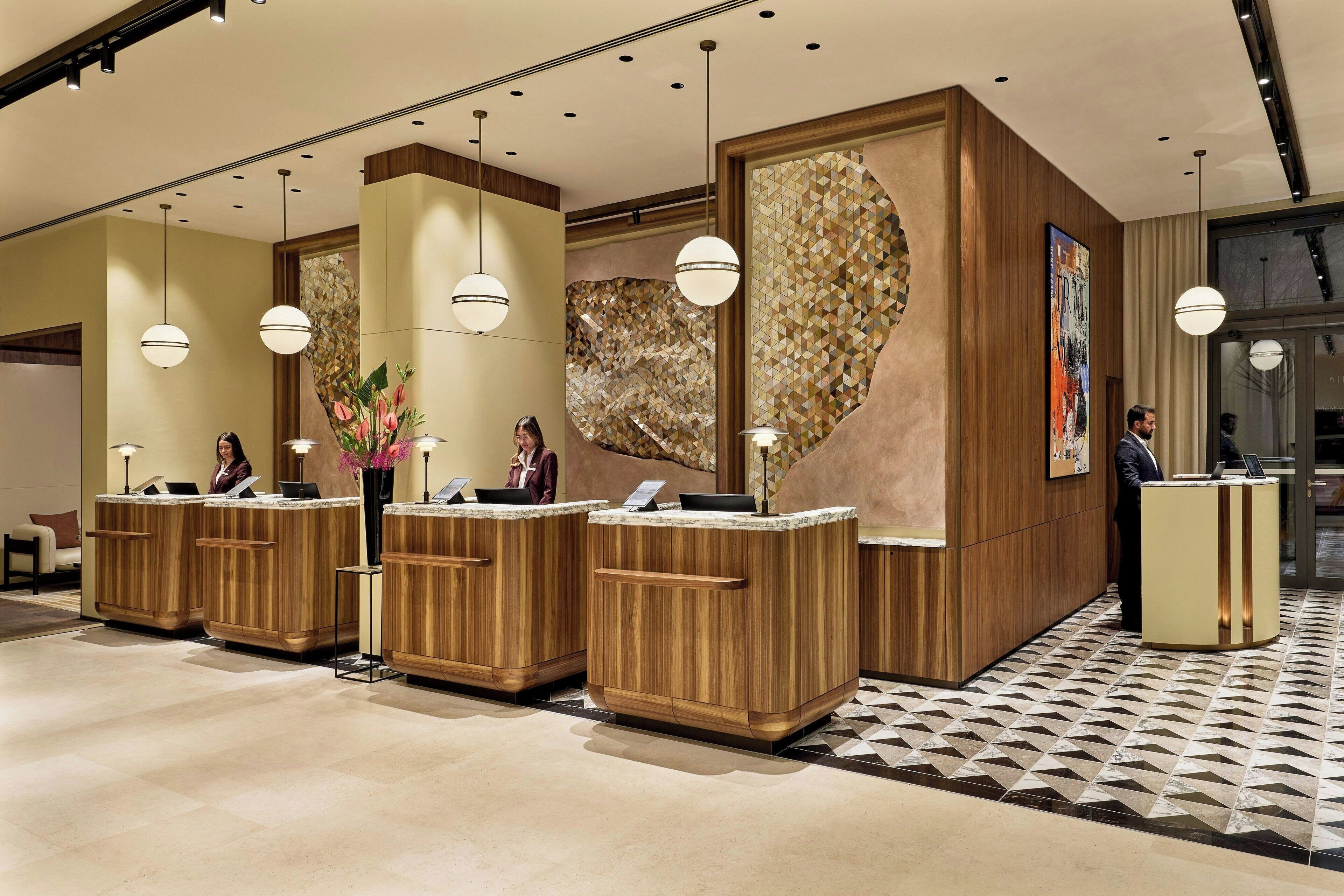 A reception area with wooden reception desks, pendant lighting, and a geometric patterned floor.