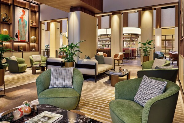A spacious lobby with green armchairs, a bar area, and a seating area with a patterned rug. - Berlin Marriott Hotel (Berlin)