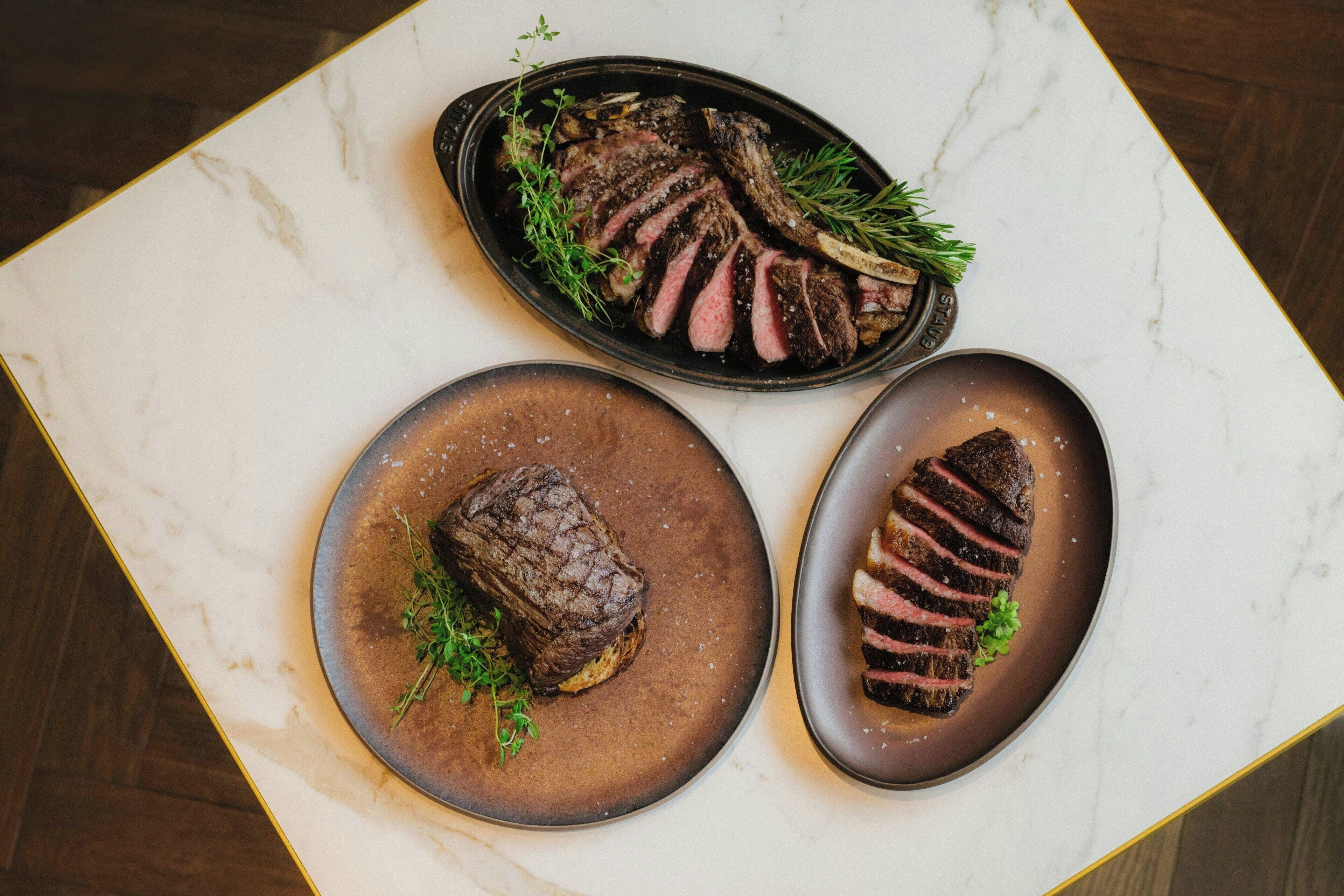 Ein Marmortisch mit drei Steaks, jedes mit Kräutern verziert.
