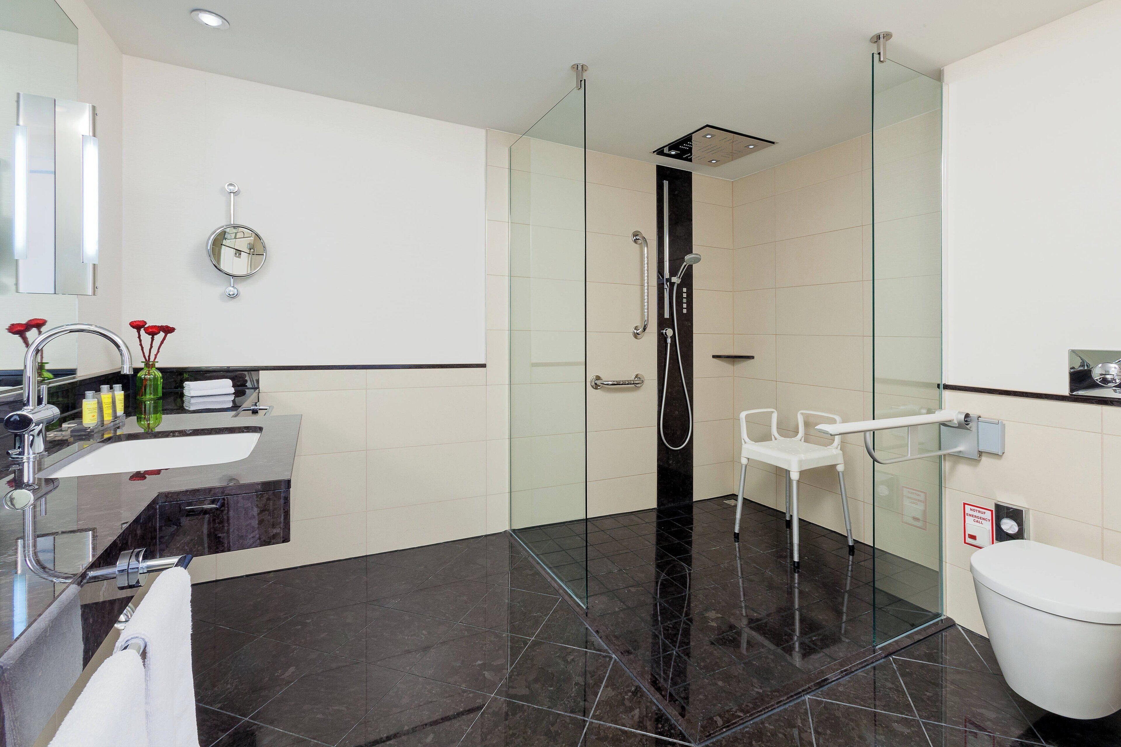 Un baño moderno con ducha de vidrio, inodoro blanco y tocador con lavamanos y espejo.