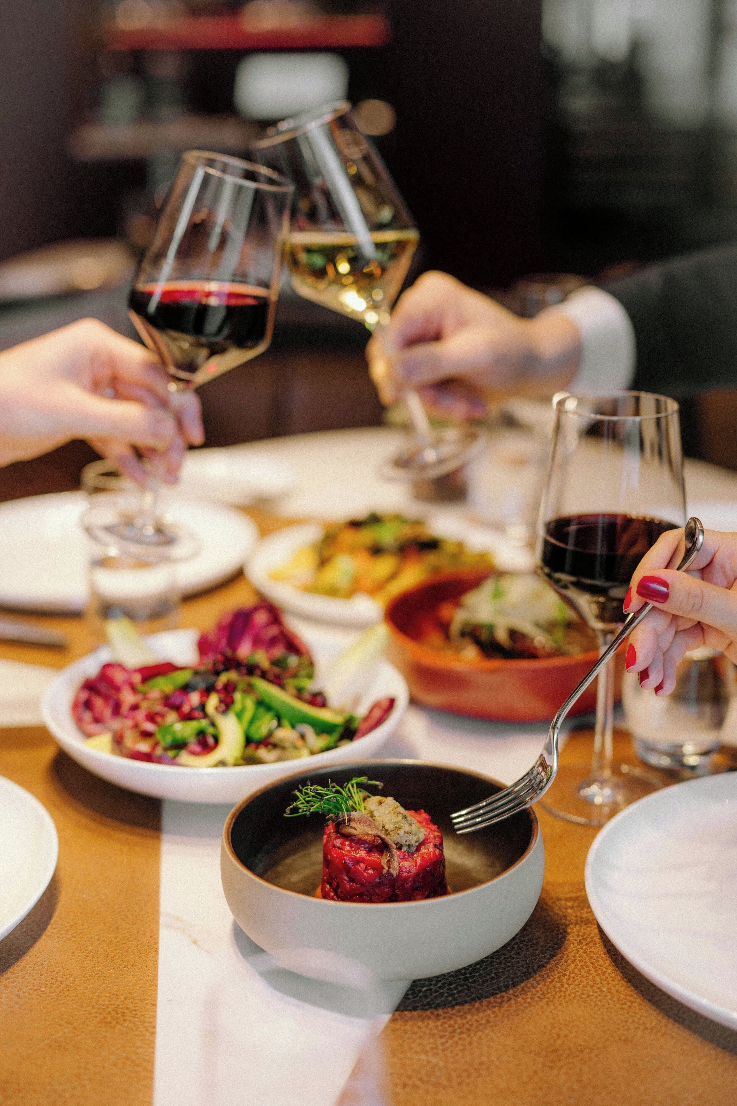 Une table à manger avec différents plats, des verres de vin et une personne tenant une fourchette.