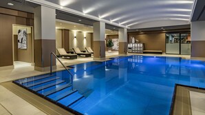 An indoor swimming pool with clear blue water, surrounded by lounge chairs and a reception area. - Berlin Marriott Hotel (Berlin)