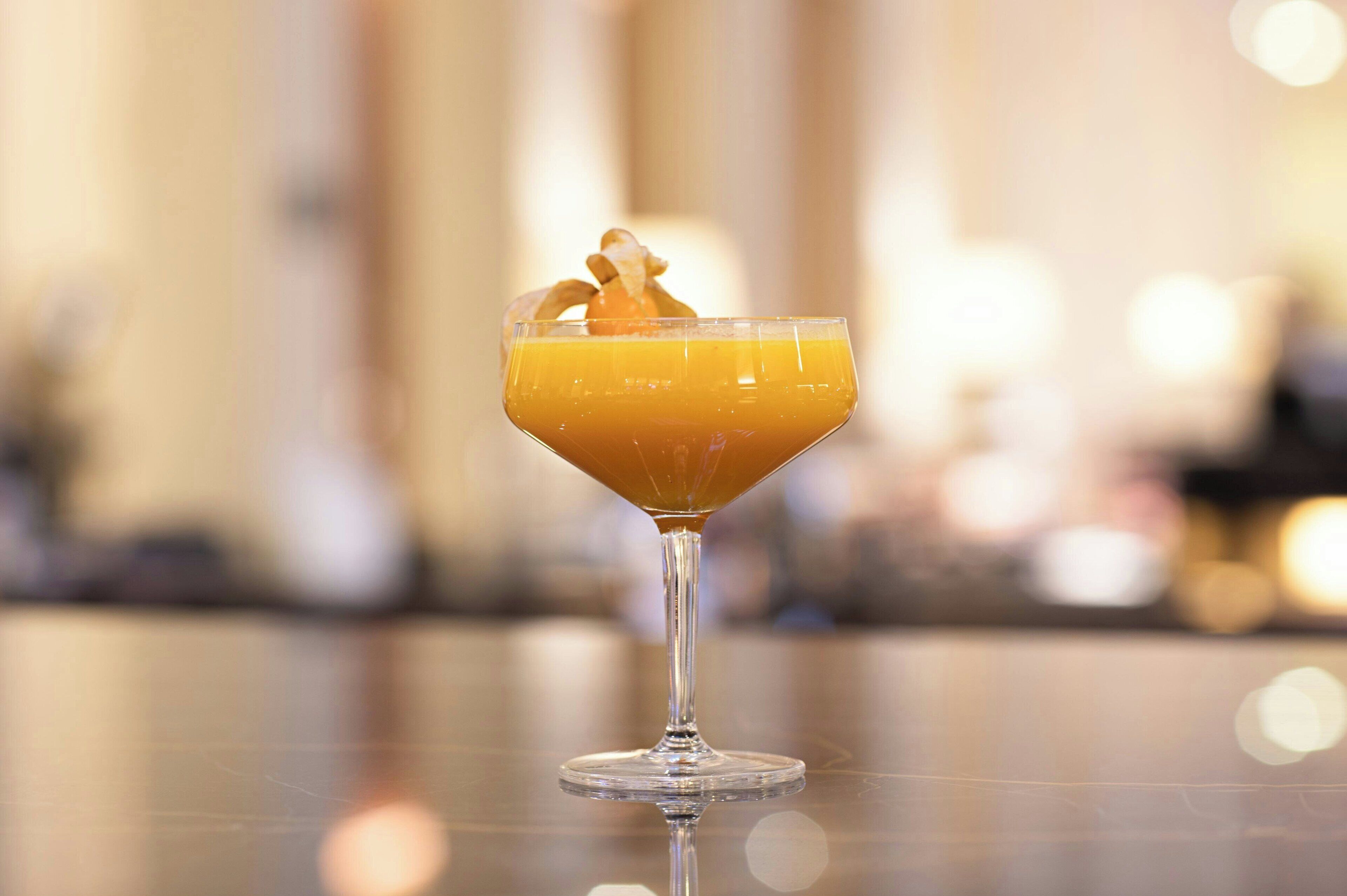 A cocktail in a martini glass with a garnish on a reflective surface.