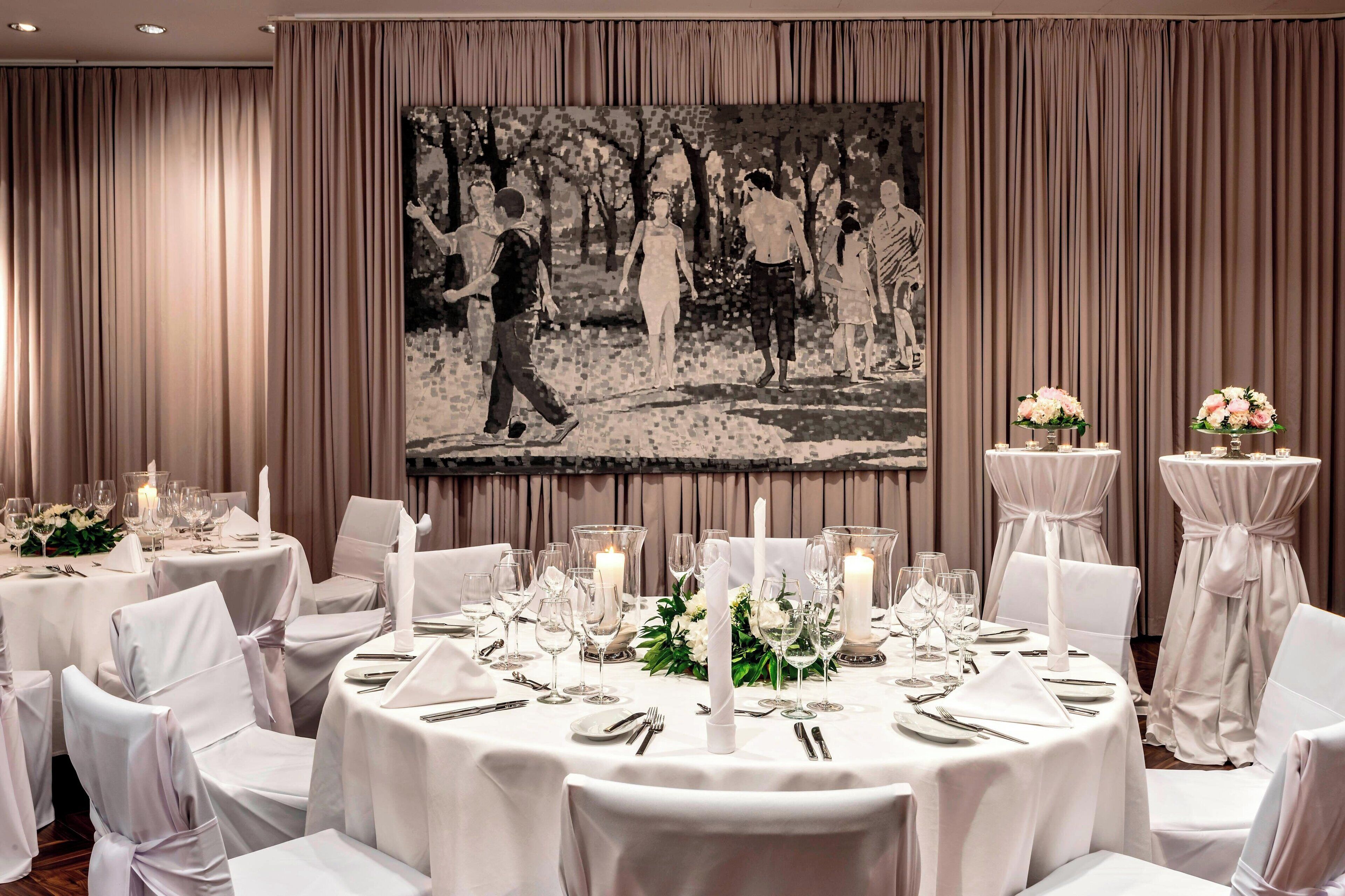A formal dining room with round tables set for a meal, featuring white tablecloths, candles, and floral centerpieces.