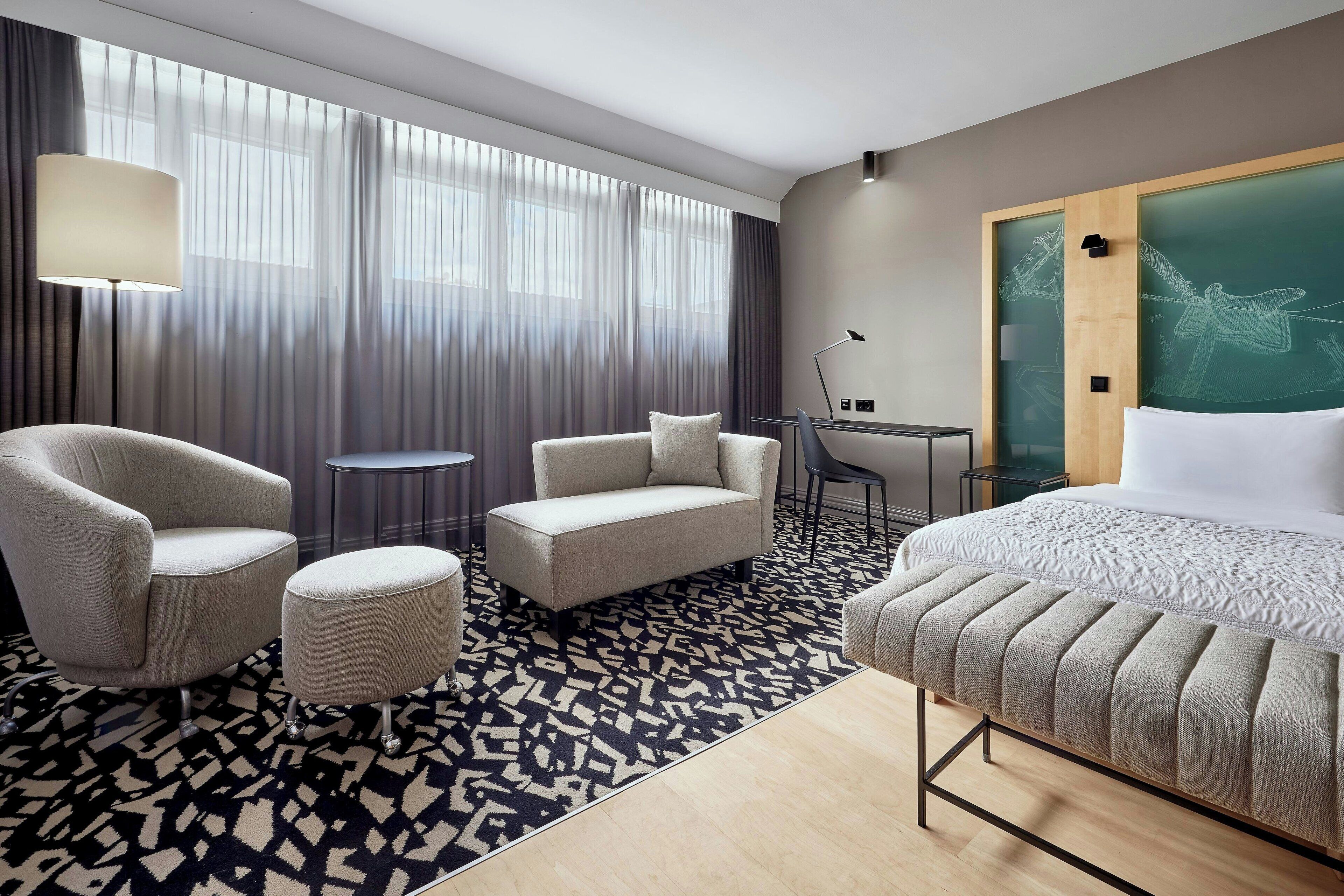 Quarto de hotel com uma cama, um sofá, uma cadeira, uma mesa pequena e um abajur.