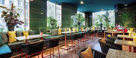 Un restaurante moderno con techos altos, amplias ventanas y diversas opciones de asientos, incluyendo cabinas y mesas.