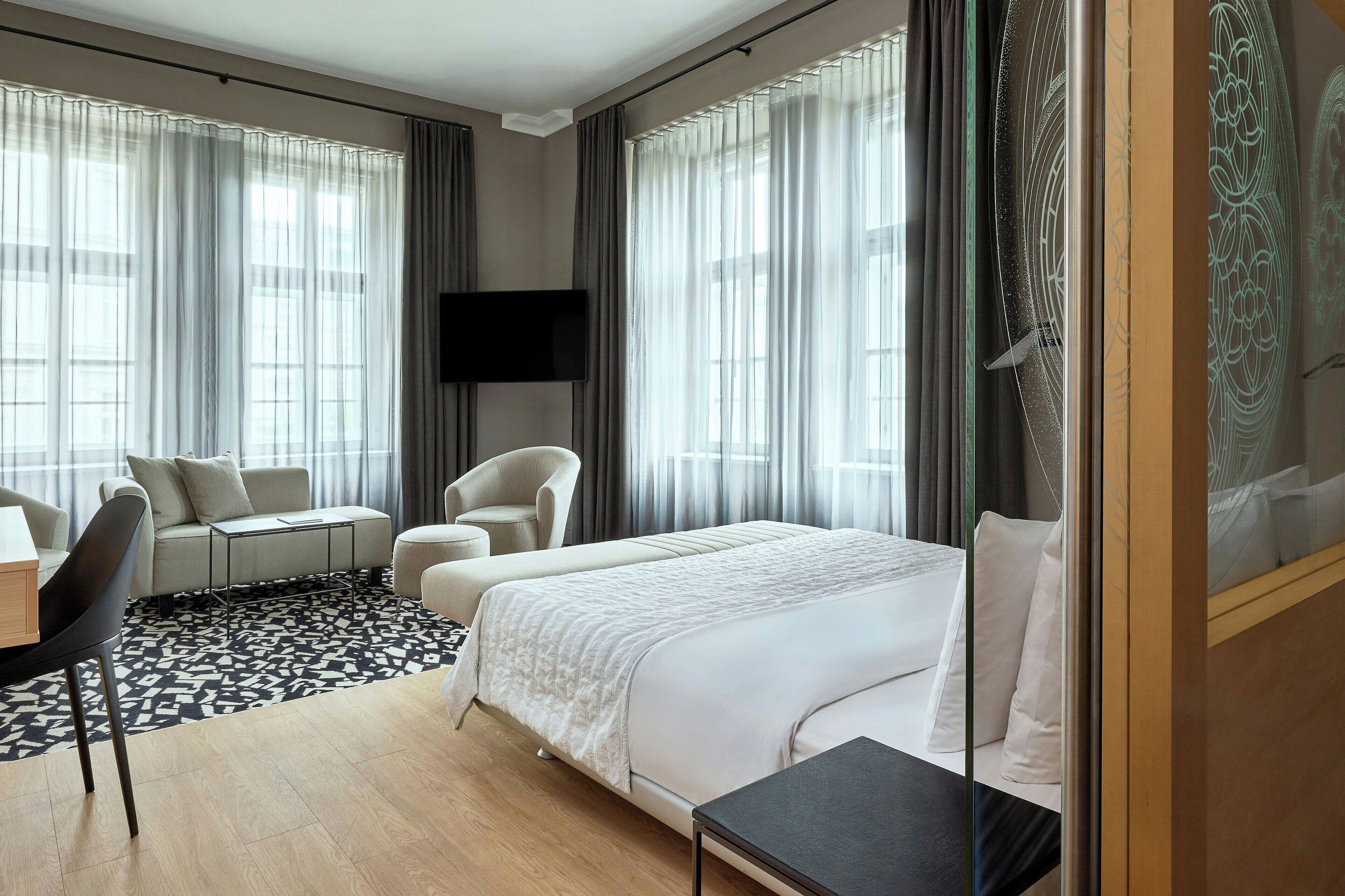 A hotel room with a bed, two armchairs, a sofa, a desk, and a TV.