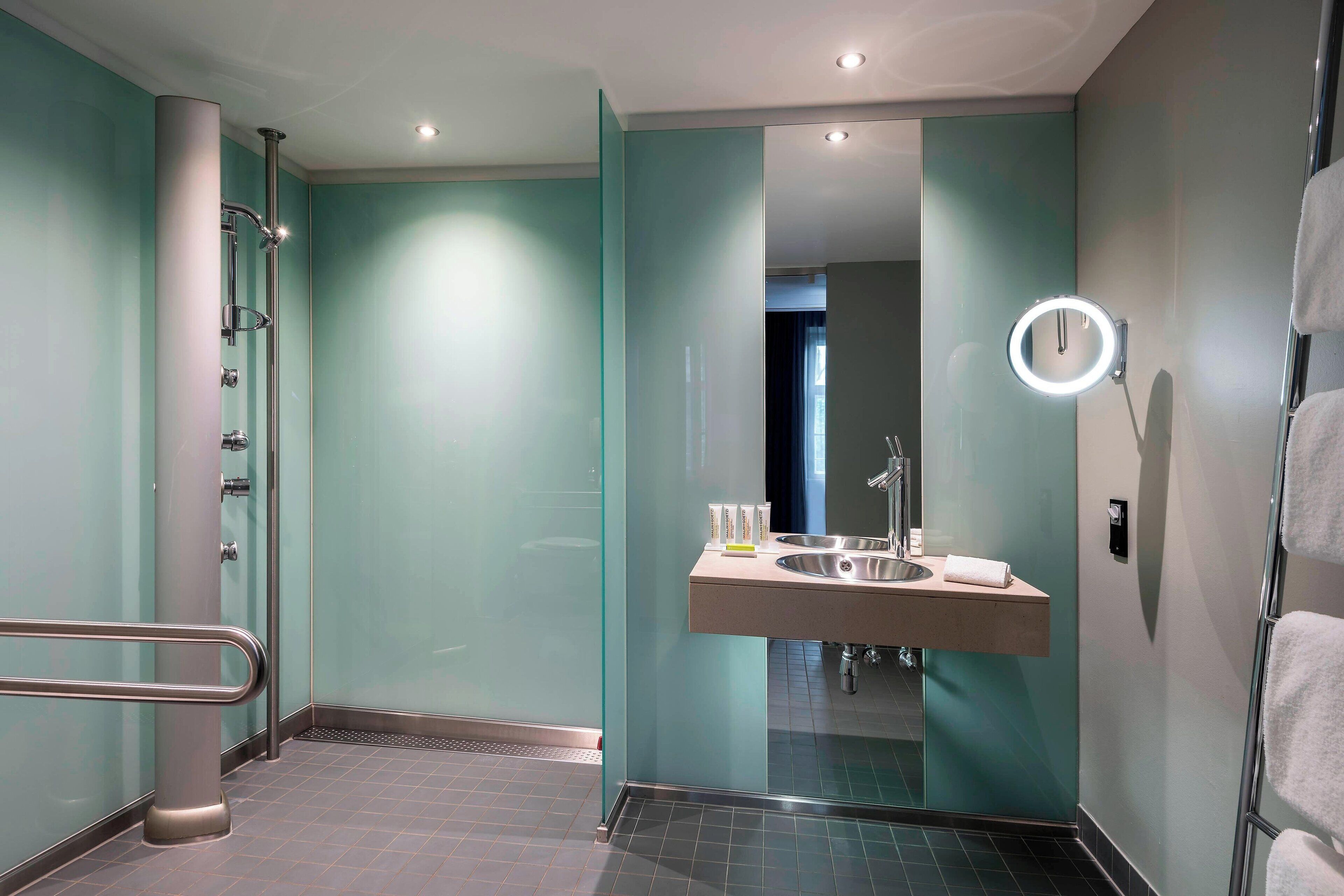 Un baño moderno con cabina de ducha de vidrio, tocador con espejo y un perchero para toallas.
