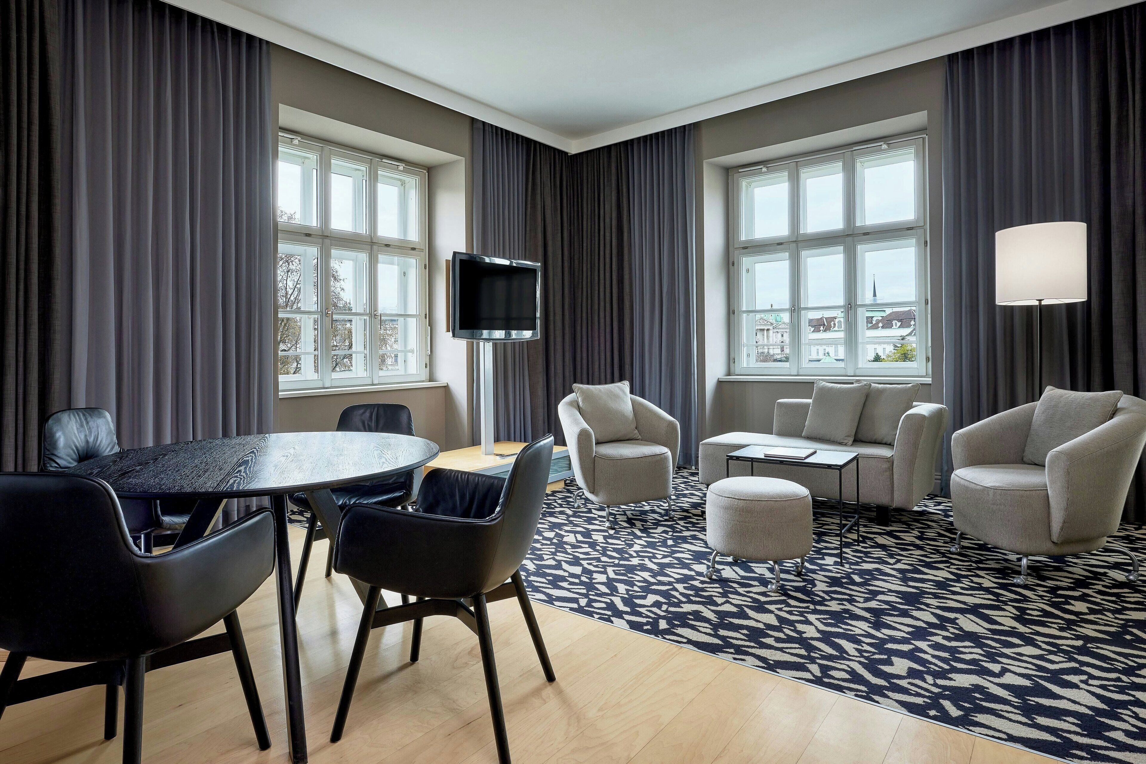 A modern hotel room with a dining area, a TV, and large windows.